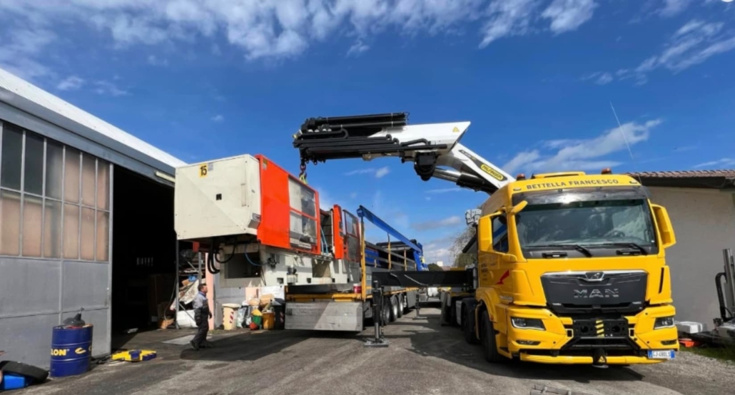 Bettella_trasporti eccezionali Camion con gru che posiziona un macchinario davanti ad un capannone